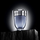 Показана е бутилка на мъжката тоалетна вода Rabanne Invictus EDT от Paco Rabanne с декоративен капак и елегантен дизайн.